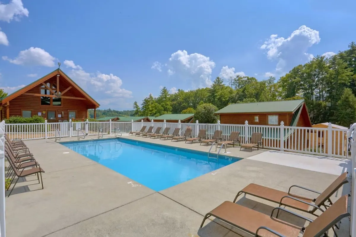 This image features a community swimming pool surrounded by lounge chairs, a log cabin building, and lush trees. The pool area exudes a leisurely and welcoming vibe, perfect for families to relax and cool off after a day exploring nearby attractions.