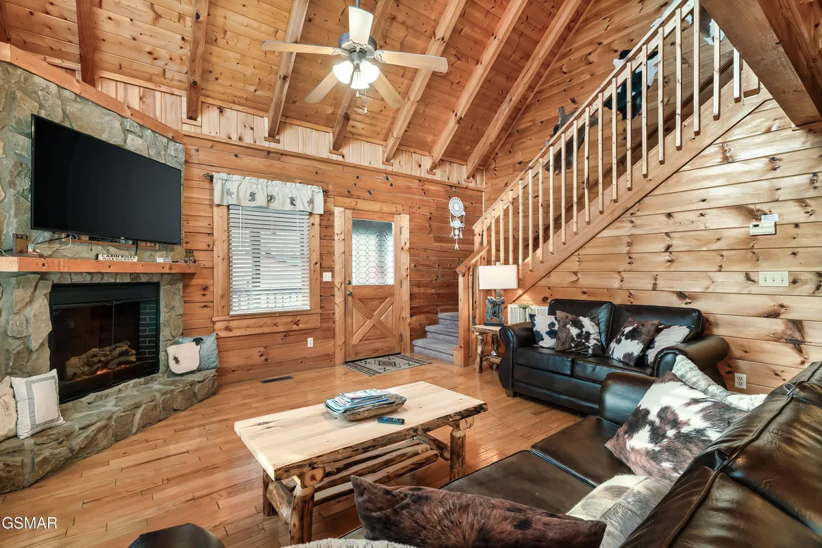 A cozy living room with a prominent stone fireplace, rustic wood beams, a leather sofa, and a coffee table perfect for gathering. The space exudes warmth and provides a comfortable area for groups to relax and reconnect.