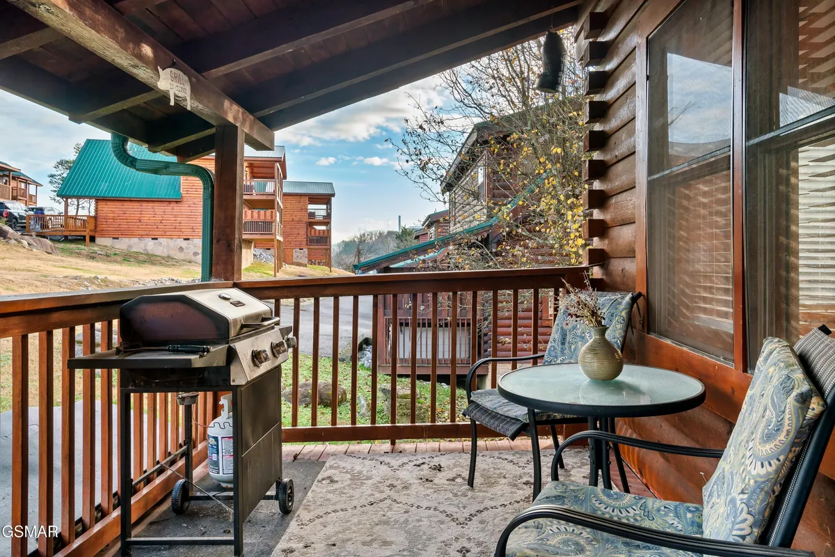This image features a cozy exterior deck with a propane grill, table and chairs, and a scenic view beyond the wooden railing. The setting invites guests to enjoy outdoor meals, morning coffee, or a relaxed afternoon surrounded by nature.