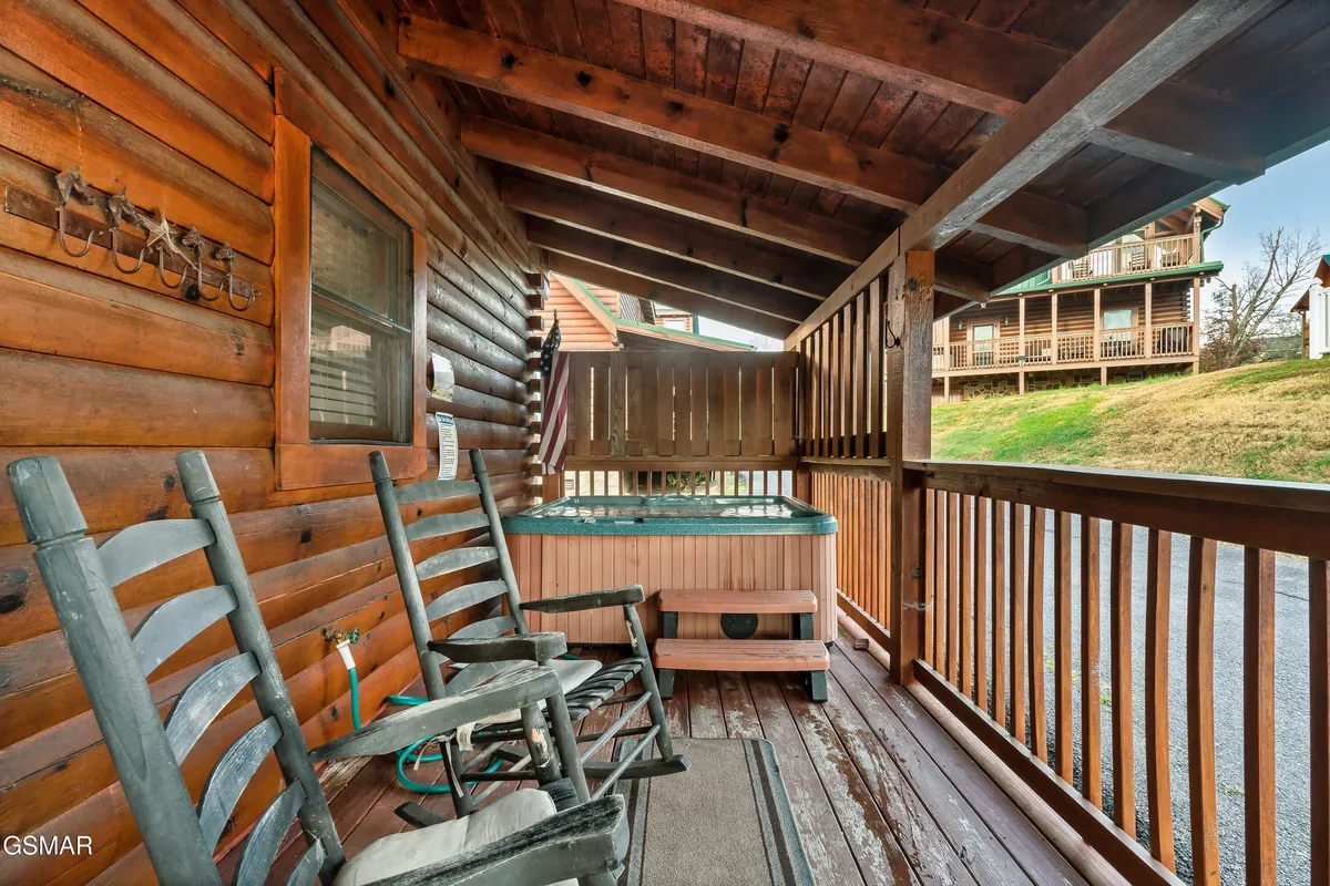 The photo shows a tranquil porch area with rocking chairs and a bubbling hot tub nestled against a wooden railing. The setting is peaceful and inviting, ideal for unwinding under the stars or enjoying a family game night on the porch.