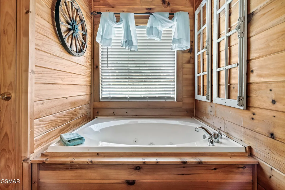 The scene features a luxurious whirlpool tub set against wooden wall paneling, with decorative elements and curtains framing a tranquil space. The tub is perfect for a relaxing soak, offering a spa-like experience within the privacy of the upper-level king suite.