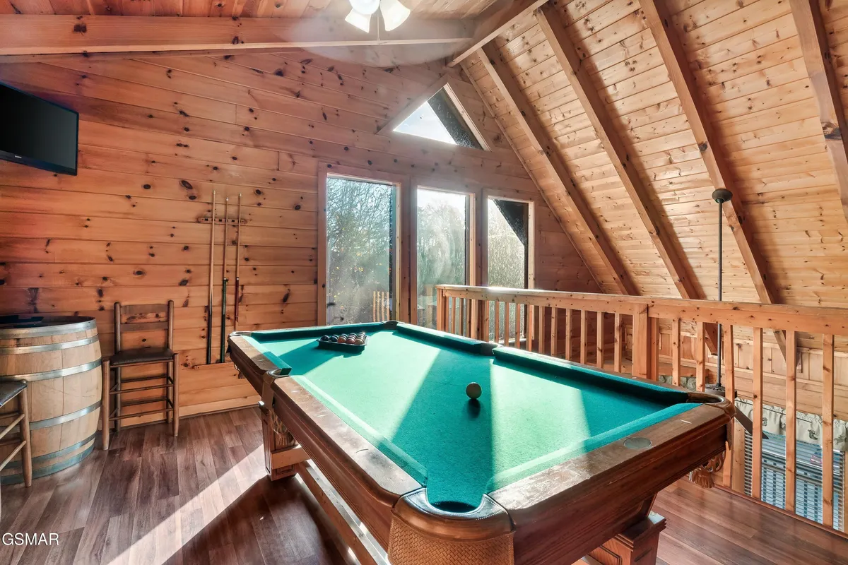 A fun, social space centered around a pool table with large windows that bring in natural light. Wooden walls and a ceiling fan add to the rustic charm, while the view to the outdoors suggests easy transitions between indoor fun and nearby attractions.