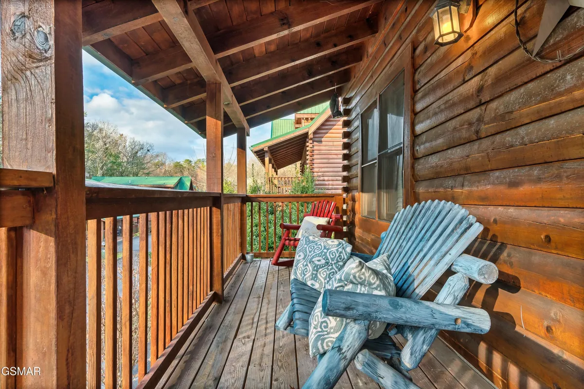 This photo captures a portion of the cabin's deck, featuring vibrant blue and red Adirondack chairs positioned to take in the surrounding trees and mountain air. The wooden railing and textured wall add rustic charm, while the setting offers a peaceful outdoor retreat for guests and their pets.
