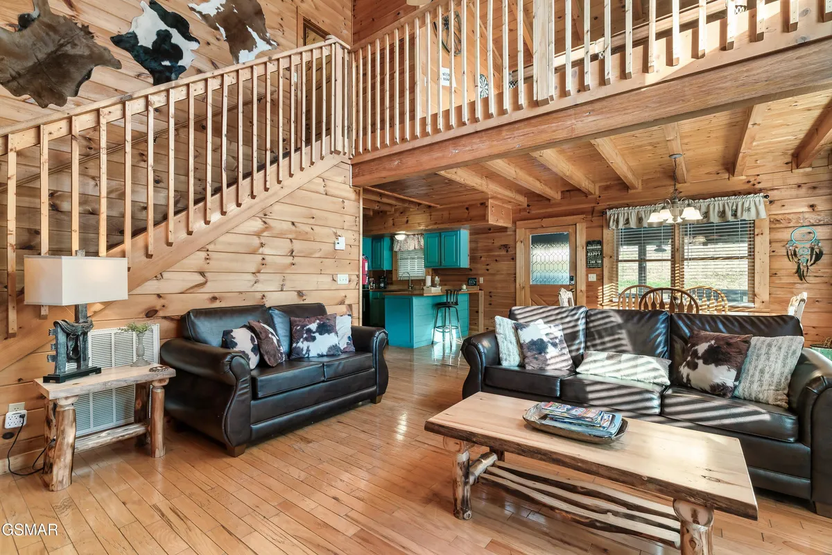 This image captures an angle of the living area that highlights a wooden staircase, sofas, a coffee table, and a view into the kitchen area. The setting is warm and welcoming, perfect for family gatherings or relaxing evenings after a day exploring.