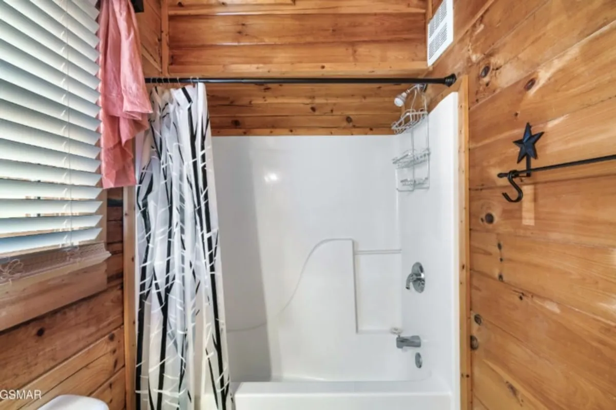 A warmly lit bathroom with a wooden tub/shower combo, wood-paneled walls, a star decoration, and a shower curtain. The space is inviting and functional, set up for self-care routines and daily refreshment.